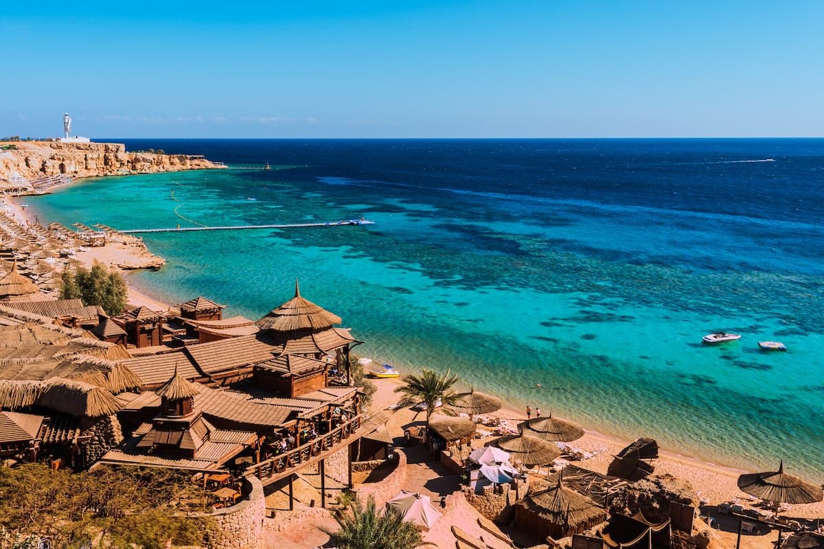 Vista aerea di una baia a Sharm el-Sheikh sul Mar Rosso — ristoranti su palafitte, acque turchesi con barriere coralline, pontili.
