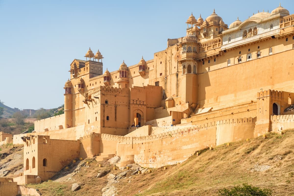 Il Forte di Amber sopra il lago Maota vicino a Jaipur in Rajasthan — mura di arenaria, cortili terrazzati e le colline degli Aravalli.